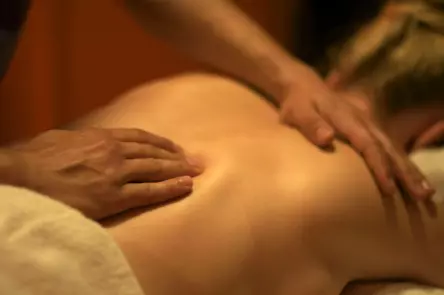 Back massage. Person laying on a couch in a harmonious, relaxing clinical setting. A pair of hands are shown applying firm pressure while massaging their back.