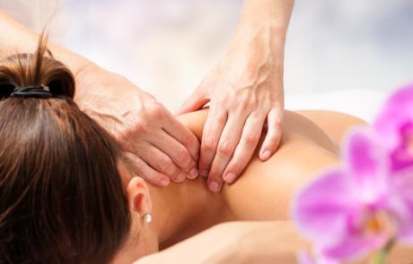 Neck massage. Person laying on a couch in a harmonious, relaxing clinical setting. A pair of hands are shown applying firm pressure while massaging their back.