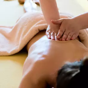 Back massage. Person laying on a couch in a harmonious, relaxing clinical setting. A pair of hands are shown applying firm pressure while massaging their back.