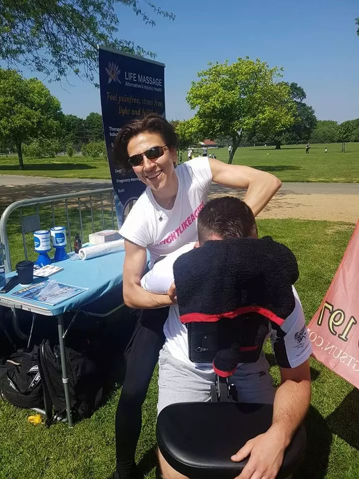 On site treatments at events. Life Massage therapist, shown while treating a person on a massage chair at an event held in a park..