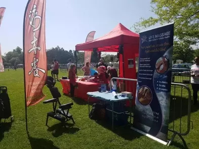 On site treatments at events. Life Massage event setting. Banner, massage chair,, table and gazebo are shown at an event held in a park.