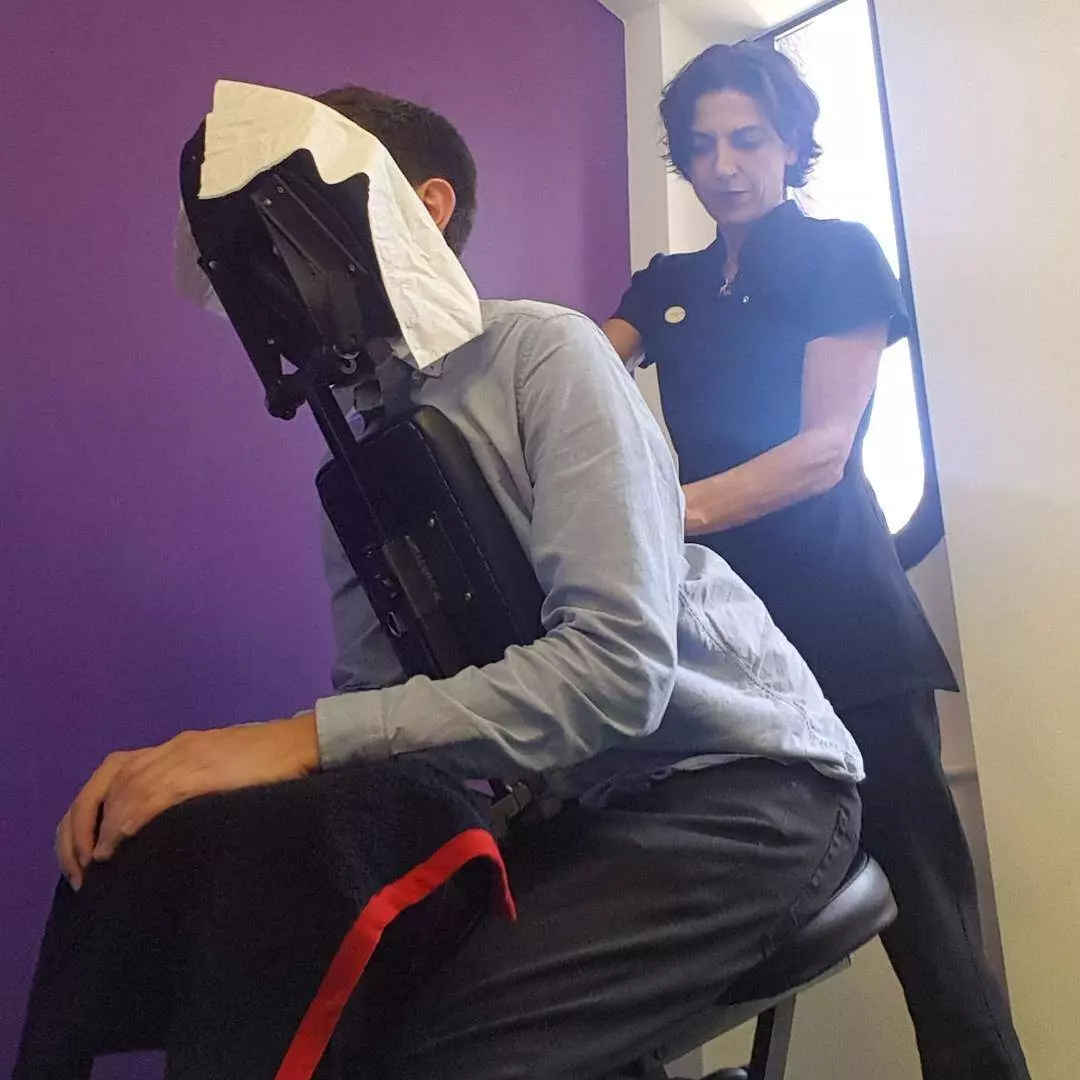 On site treatments in companies. Life Massage therapist, shown while treating a person on a massage chair in a company on site.